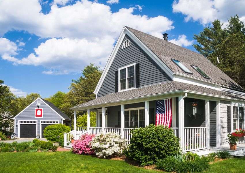 A Denton gray paneled single-family home with an american flag is pictured on a bright green stretch of lawn.
